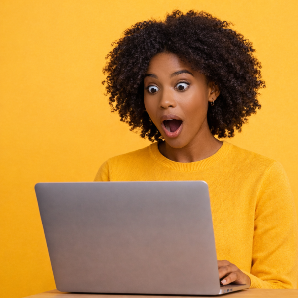 Femme surprise devant son ordinateur portable, réaction étonnée et positive sur fond jaune.